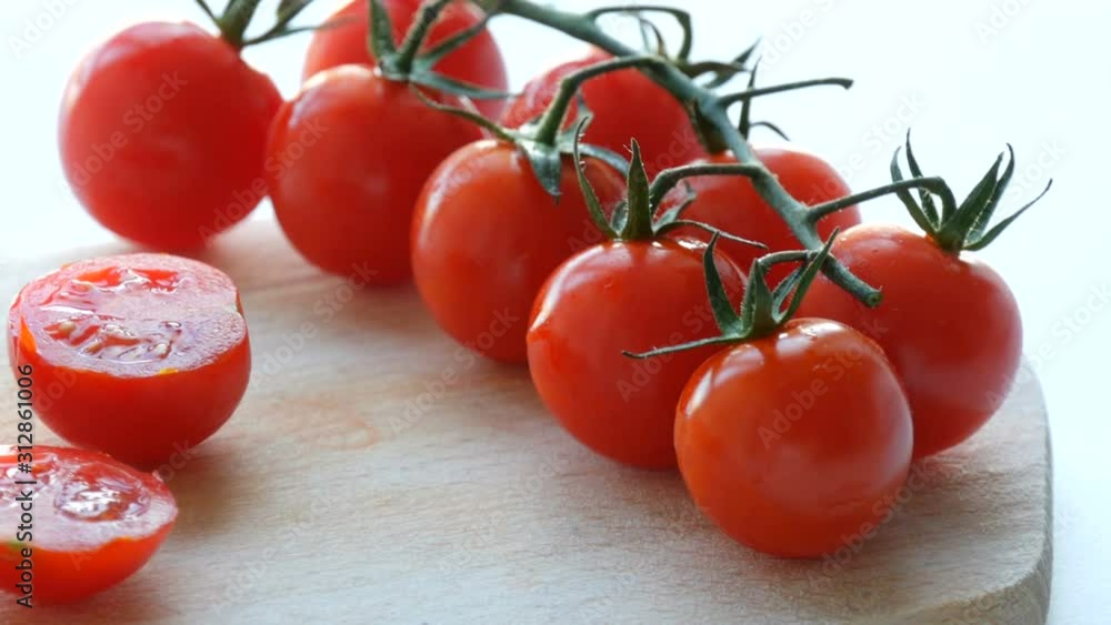 Beautiful juicy ripe cut red cherry tomatoes in clusters on a white table background and wooden kitchen board Beautiful juicy ripe cut red cherry tomatoes in clusters on a white table background and wooden kitchen board