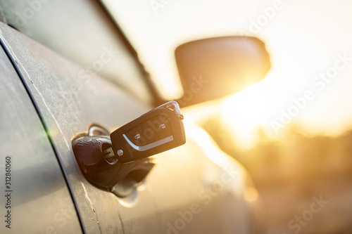 Car keys were plugged into the silver car door at outdoor parking lot with sunlight effect in morning or sunset time