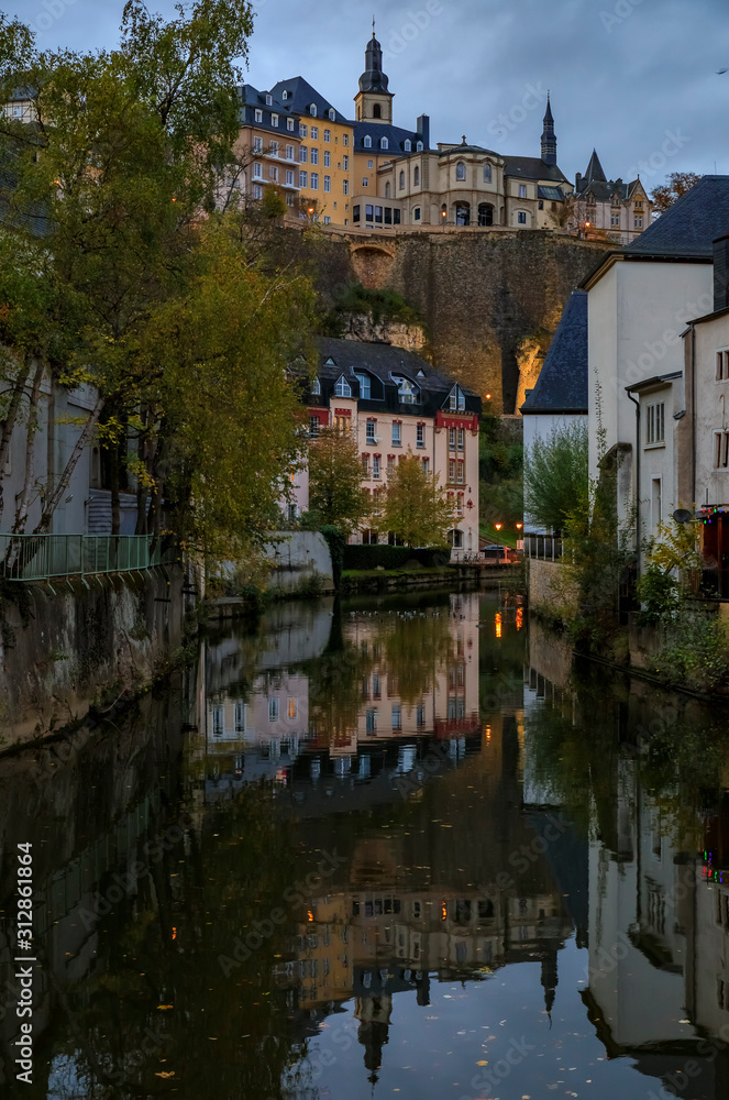 Pastel houses reflecting in Alzette river in Luxembourg old town, UNESCO World Heritage Site and the city wall at sunset