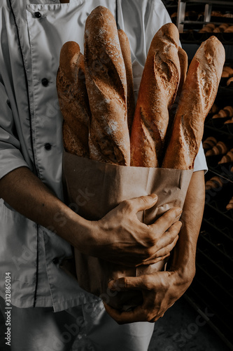 baker's hands are holding a craft baguette with baguettes on a dark background