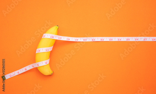 Print op canvas Yellow banana with measurement tape on orange background