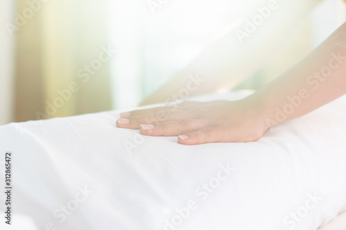 Hand of housekeeper set up white pillow on the bed sheet in hotel room at morning time with sunlight from windows