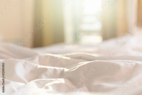 White bedding sheets and pillow in hotel room at morning time with sunlight from windows photo