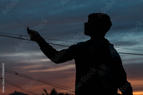 Silhouette of a little kid flying kite during sunset