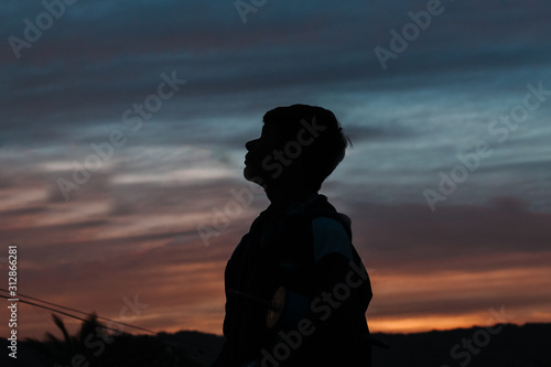 Silhouette of a young Indian boy looking up towards the sky during the sunset at Wankaner, Gujarat, India