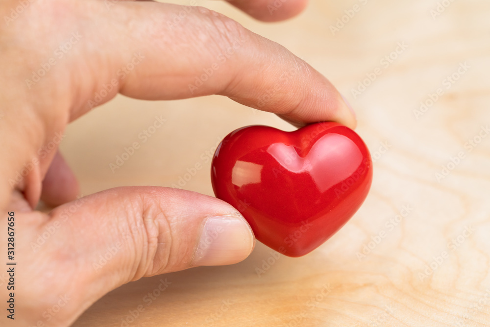Hand holding red heart shape with fingers on wooden background using as love symbol, health care, happy relationship or Valentine day event Hand holding red heart shape with fingers on wooden background using as love symbol, health care, happy relationship or Valentine day event