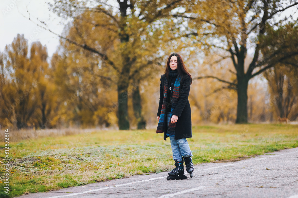 A pretty young girl in a coat and with a long scarf happily skates in the autumn park. Fighting the autumn depression. To overcome depression. A pretty young girl in a coat and with a long scarf happily skates in the autumn park. Fighting the autumn depression. To overcome depression.