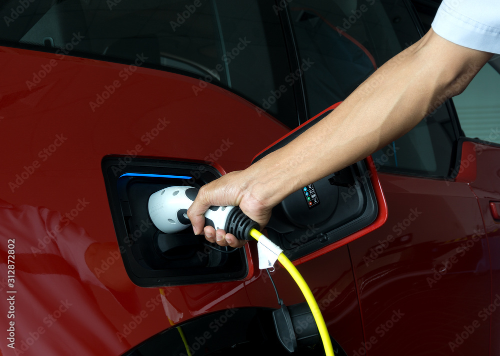 Hand of man holding plug for charge electric power into Battery of Electric car on charge station electric mobility environment friendly with copy space. Hand of man holding plug for charge electric power into Battery of Electric car on charge station electric mobility environment friendly with copy space.