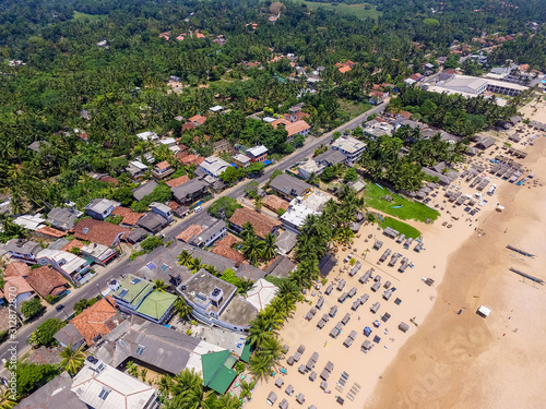 Beach and palm trees with coconuts on beach in Hikkaduwa, Sri Lanka.  Aerial view of town of Hikkaduwa with its beaches, surfspots and buildings. Beautiful tropical beach with great waves for surfing. photo