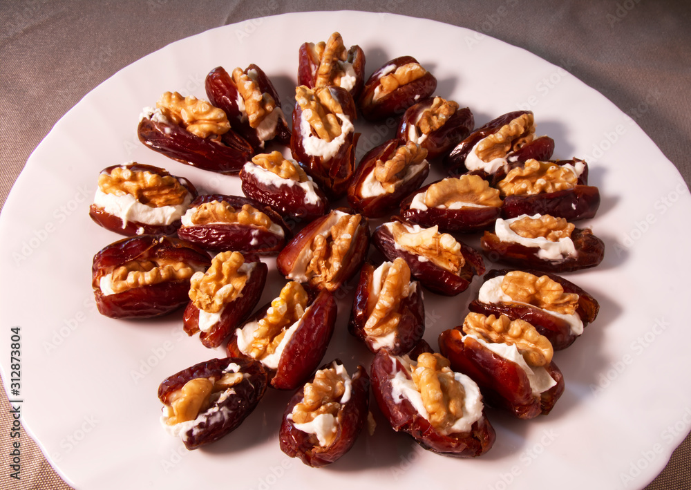 Fresh dates filled with mascarpone cheese and walnuts in a white dish. Fresh dates filled with mascarpone cheese and walnuts in a white dish.
