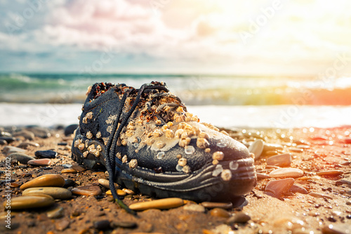 Concept of environmental protection and pollution. An old Shoe, covered with shells, lies on the shore. In the background, the waves of the ocean. Copy space. Sunlight