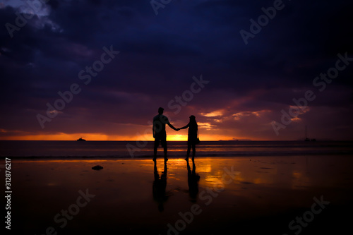 Silhouette of couple hold each other hand and Happy Young Couple love on the beach at sunset time