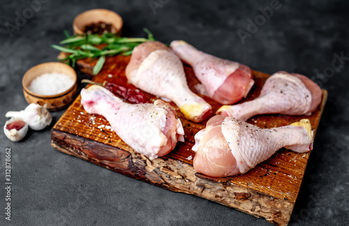  raw chicken legs with spices on a cutting board on a stone background