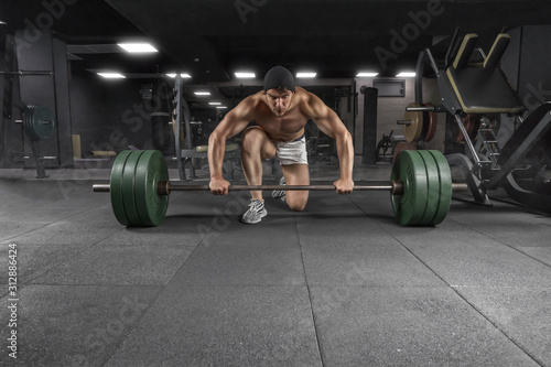 Front view of power athletic guy standing with barbell workout in the gym photo