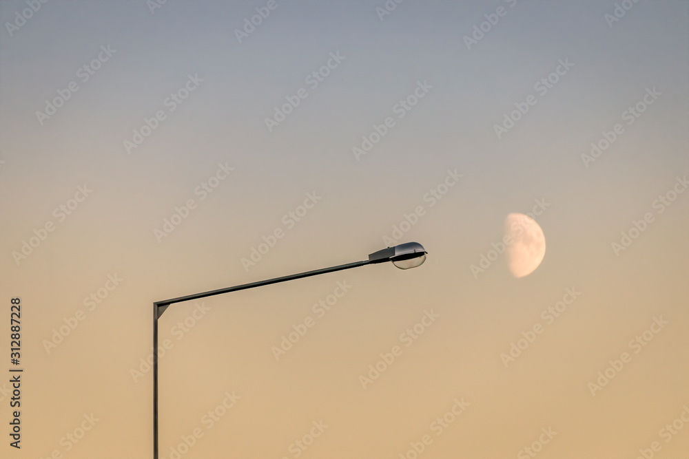 Streetlamp and a first quarter moon against an evening sky Streetlamp and a first quarter moon against an evening sky