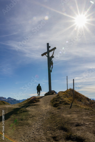 Silhouette of a Christian cross on the hill and a man walking towards it on a blue sky with sun halo