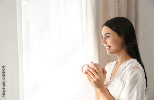 Young woman with cup of coffee near window. Lazy morning