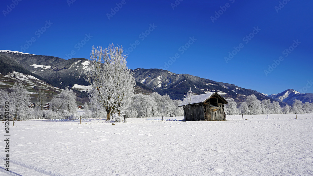 a wood hut on a agriculture field in winter with fresh snow and a blue clear sky with view to the mountains a wood hut on a agriculture field in winter with fresh snow and a blue clear sky with view to the mountains