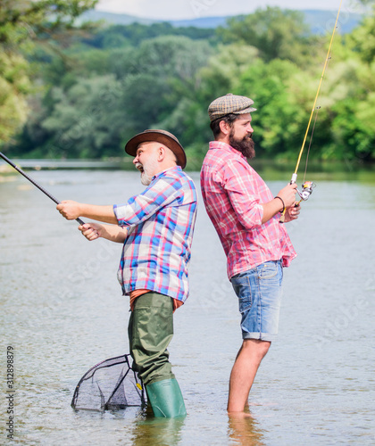 generations. summer weekend. mature men fisher. male friendship. family bonding. hobby and sport activity. Trout bait. father and son fishing. two happy fisherman with fishing rod and net