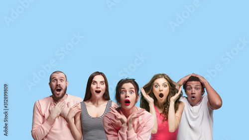 Portrait of multiethnic group of young people isolated on blue studio background, flyer, collage. Concept of human emotions, facial expression, sales, advertising. Shocked, astonished, wondered crazy.