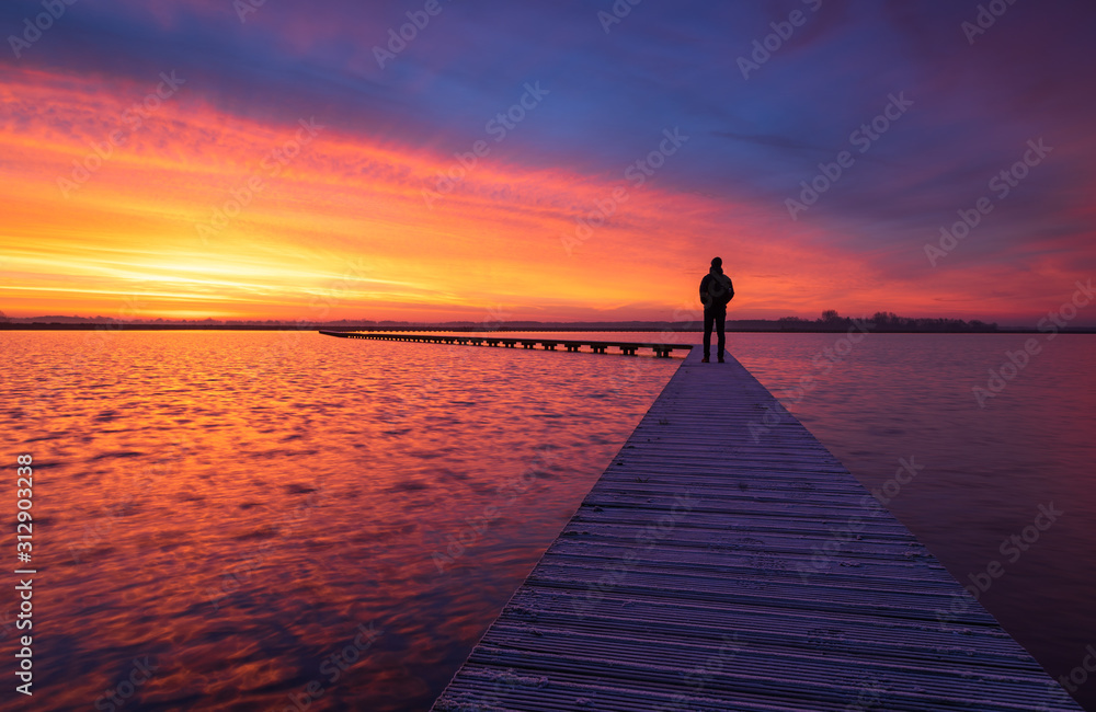 A man enjoying the colorful  dawn on a jetty in a lake. Groningen, Holland. - obrazy, fototapety, plakaty 