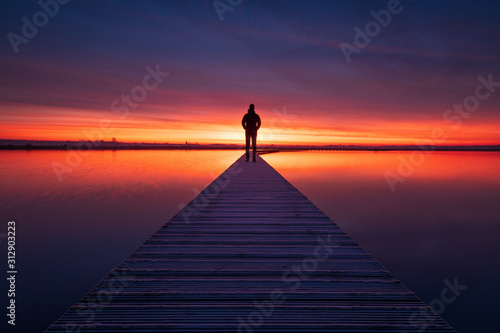 A man enjoying the colorful  dawn on a jetty in a lake. Groningen, Holland. photo