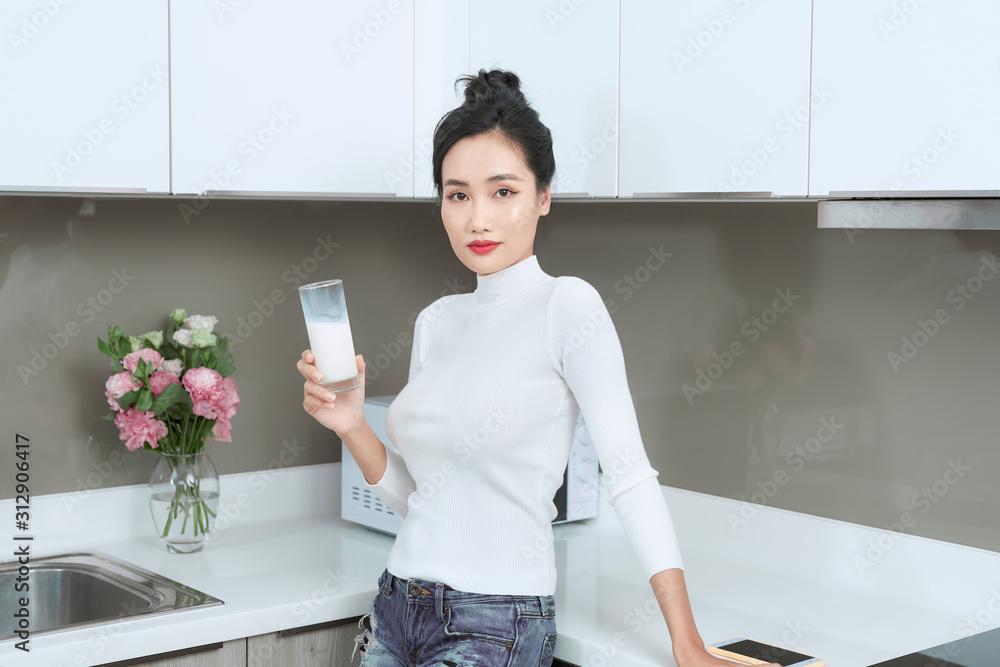 Portrait of young woman standing in kitchen while drinking milk. Portrait of young woman standing in kitchen while drinking milk.