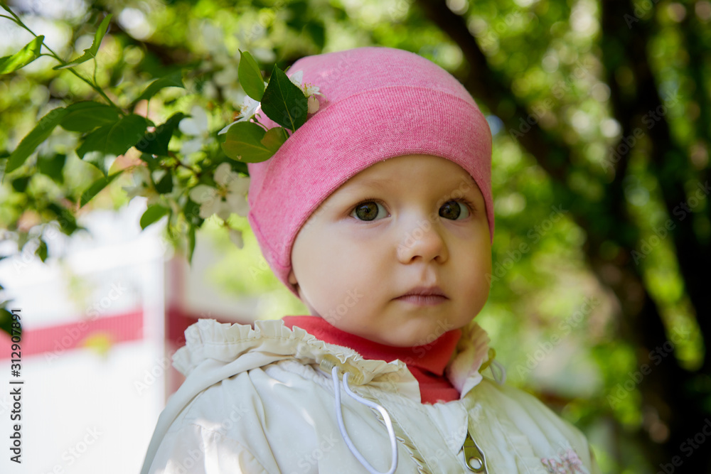 Portrait of a small girl in white dress and red hat in the park full of apple blossom trees in a spring day Portrait of a small girl in white dress and red hat in the park full of apple blossom trees in a spring day