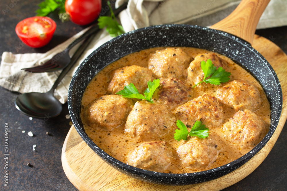 Meatballs in sour cream and tomato sauce in a pan on a dark stone or slate table.