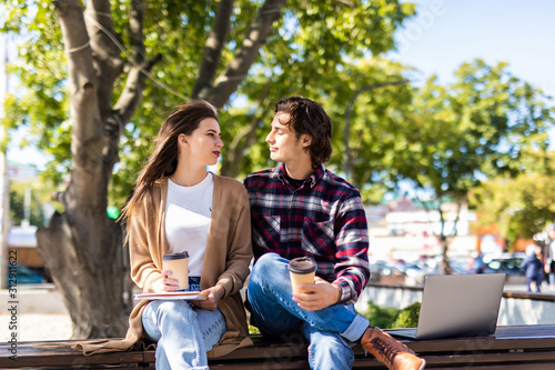 Beautiful loving couple sitting on the bench in the park, drinking coffee and having fun. Love and tenderness, relationships, fashion, lifestyle concept