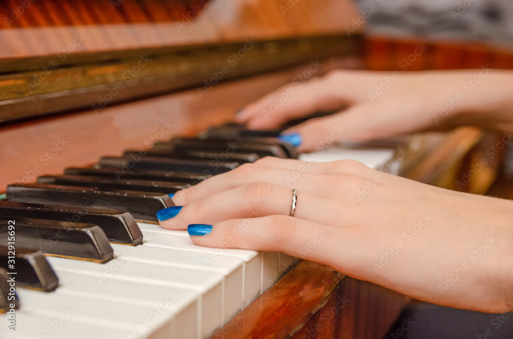 Fototapeta premium hands of a female pianist with blue nail Polish on the nails on the keys of a piano. girl playing the piano.