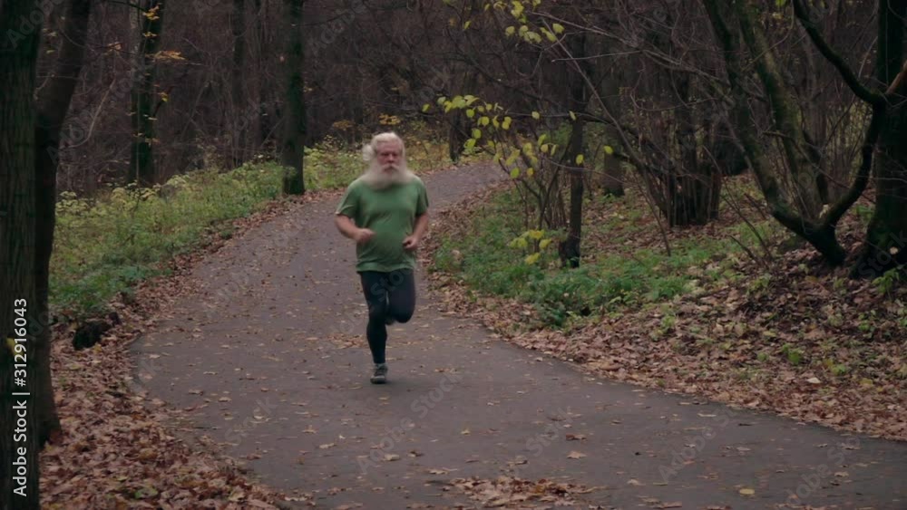 Senior man in green T-shirt runs on autumn cross country track in extreme slow motion. Senior man in green T-shirt runs on autumn cross country track in extreme slow motion.
