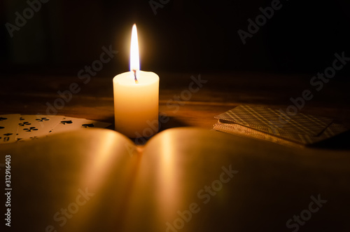 mystical atmosphere, cards, a book, a lighted candle in the dark on a wooden table. Esoteric concept, fortune telling and predictions