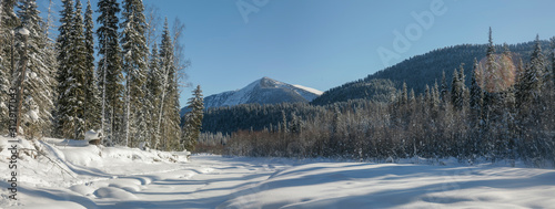 Panoramic view of a mountain valley. Winter forest, snow-capped mountain peaks. Wild place in Siberia.