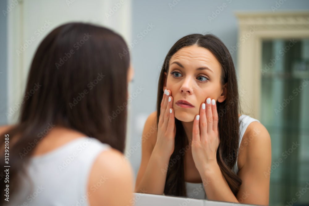 Tired woman looking at her eye bags in the bathroom. Tired woman looking at her eye bags in the bathroom.