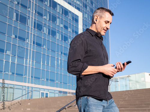 Handsome middle aged business man walking in modern city street, using his phone handsfree, daylight © Naglagla