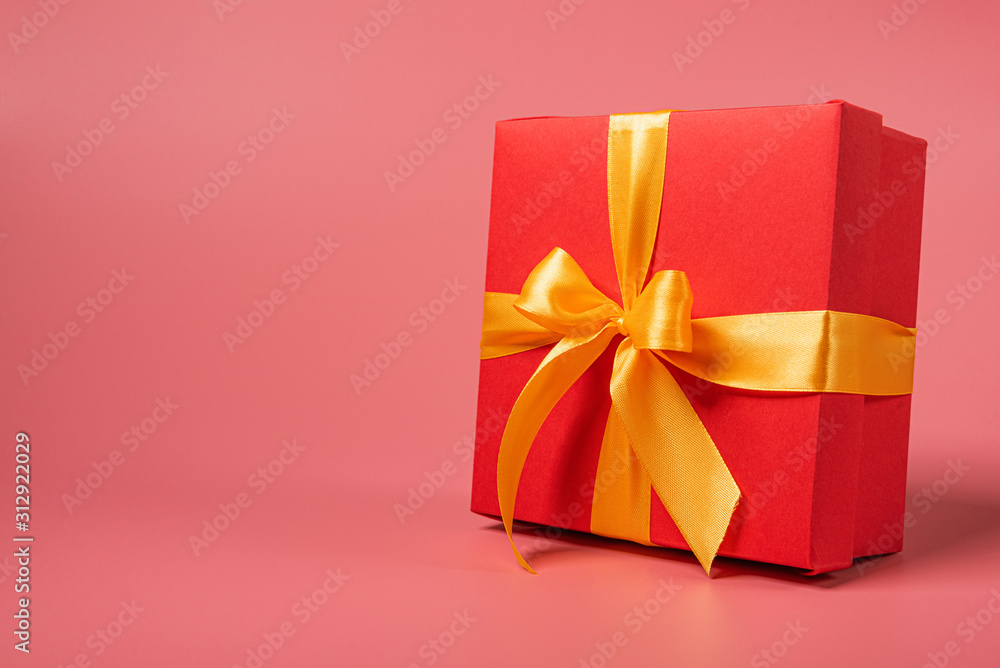 red box tied with a gold ribbon. the ribbon is tied on a box in the form of a beautiful bow. holiday gift concept