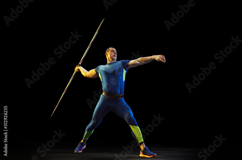 Male athlete practices in throwing javelin on black background in neon light. Professional sportsman training in action, motion. Concept of healthy lifestyle, movement, activity, competition