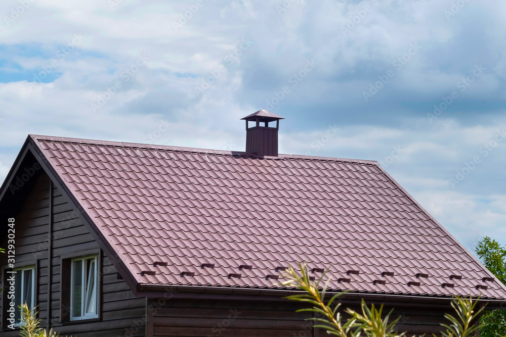 Brown tile roof with chimney against the blue sky.