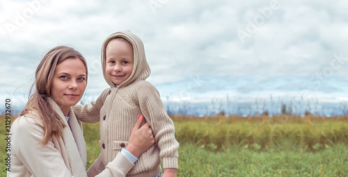 Woman mom hugs son, little boy warm casual clothes, beige sweater. Emotions tenderness caring for love, parent support, happiness, relaxation. On street autumn park field. Free space for copy text.