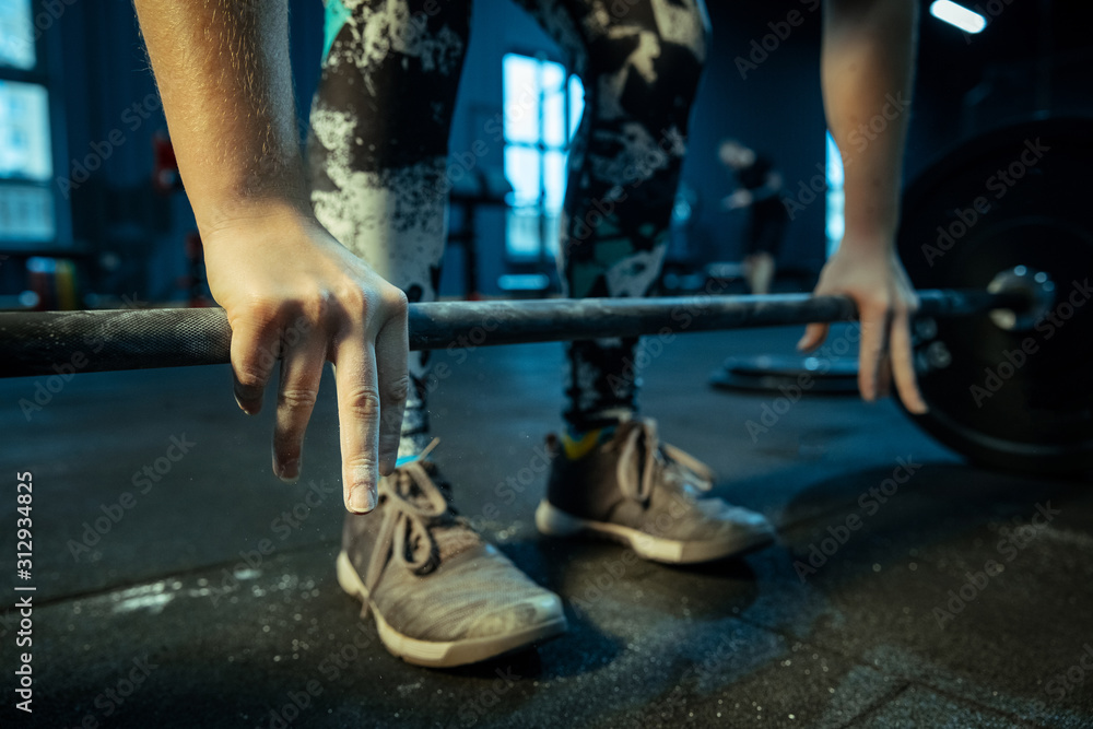 Caucasian teenage girl practicing in weightlifting in gym. Female sportive model training with barbell, looks concentrated and confident. Body building, healthy lifestyle, movement and action concept. Caucasian teenage girl practicing in weightlifting in gym. Female sportive model training with barbell, looks concentrated and confident. Body building, healthy lifestyle, movement and action concept.