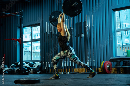 Caucasian teenage girl practicing in weightlifting in gym. Female sportive model training with barbell, looks concentrated and confident. Body building, healthy lifestyle, movement and action concept.