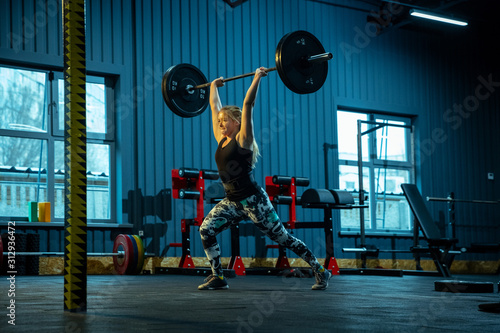Caucasian teenage girl practicing in weightlifting in gym. Female sportive model training with barbell, looks concentrated and confident. Body building, healthy lifestyle, movement and action concept.