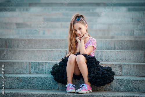 A beautiful girl in a fluffy black skirt tutu and pink sneakers sits on the steps. photo