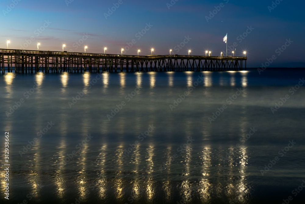 Lamp lights reflected in the ocean water below the Ventura Pier as dawn adds colors to the morning sky.