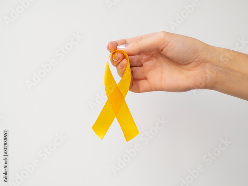 Gold ribbon hanging on fingers on white background. International Childhood Cancer Day concept