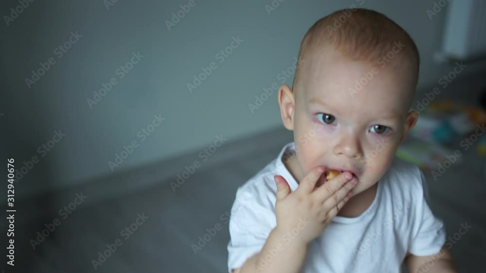 Two-year-old blue-eyed toddler eats cookies. A boy in a white T-shirt, a close photo at home, a happy childhood Two-year-old blue-eyed toddler eats cookies. A boy in a white T-shirt, a close photo at home, a happy childhood