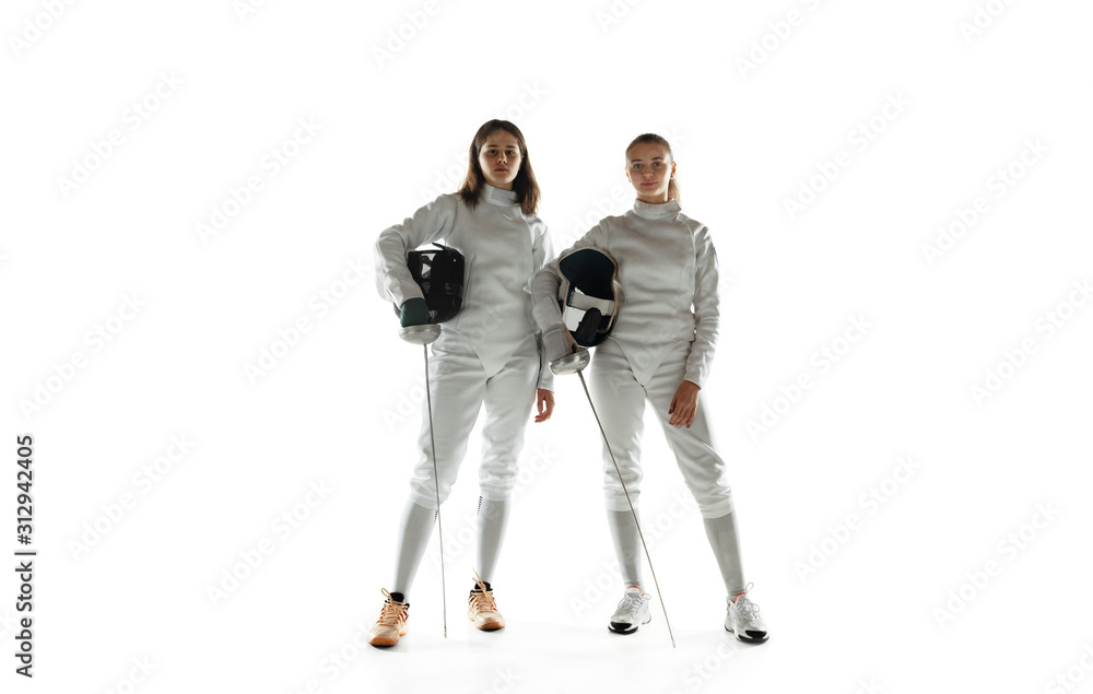 Teen girls in fencing costumes with swords in hands isolated on white studio background. Young female models training, posing confident. Copyspace. Sport, youth, healthy lifestyle, motion, action. Teen girls in fencing costumes with swords in hands isolated on white studio background. Young female models training, posing confident. Copyspace. Sport, youth, healthy lifestyle, motion, action.