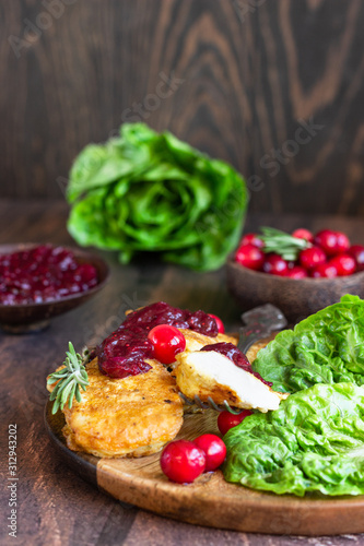 Traditional Viennese chicken schnitzel served with cranberry sauce and green salad. Wooden background. Chicken steak in breading, sauce and fresh salad. 