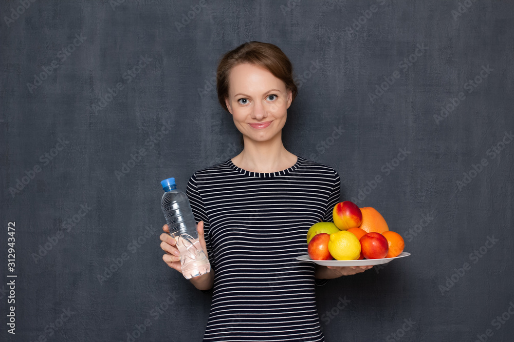 Portrait of happy woman holding plate of fruits and bottle of water Portrait of happy woman holding plate of fruits and bottle of water